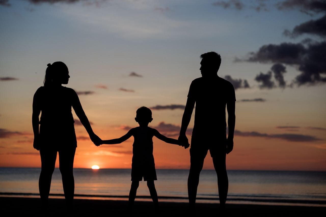 A silhouette of a family holding hands on a beach during a beautiful sunset.